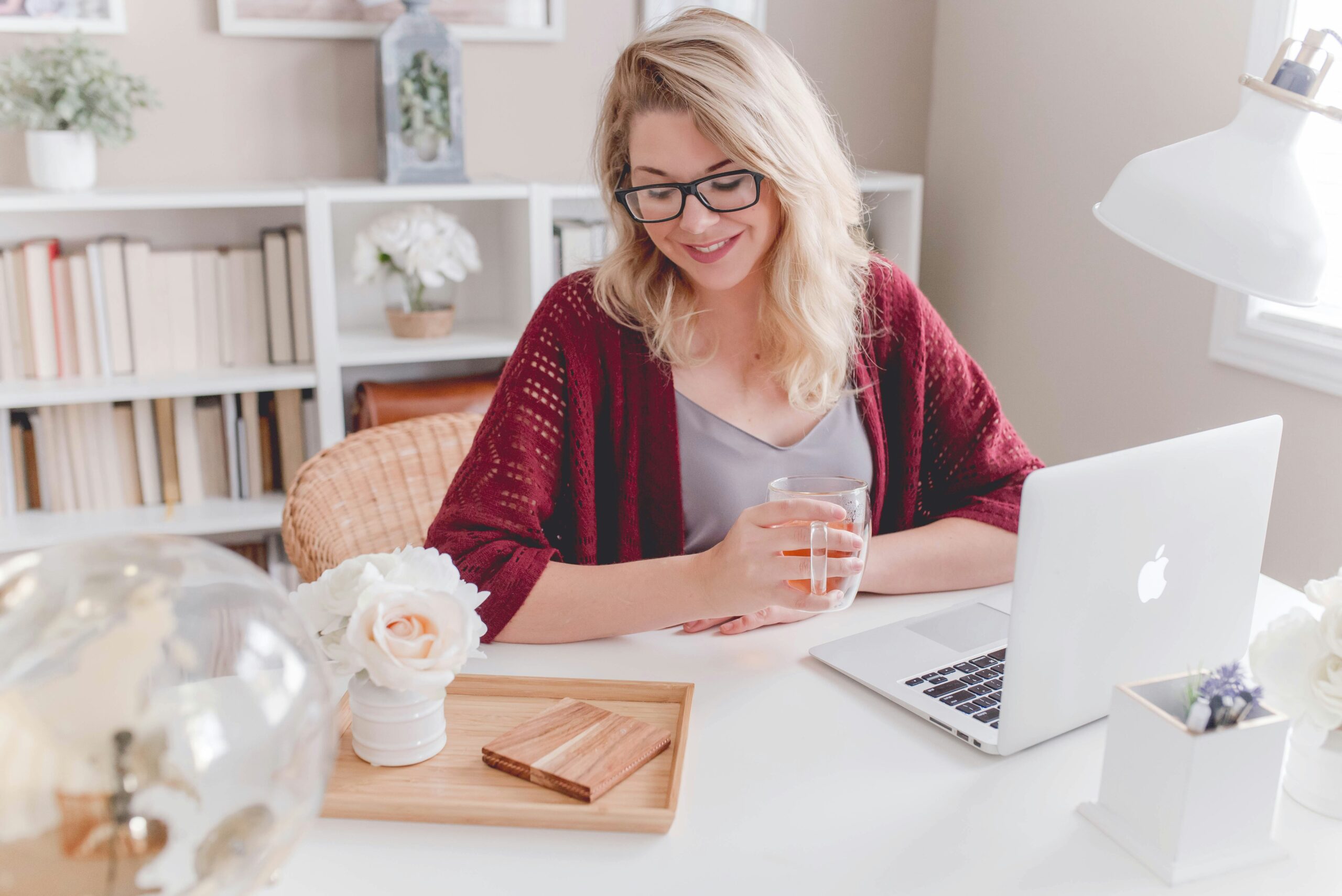 blond woman wearing glasses sitting at desk in home office with laptop and decor